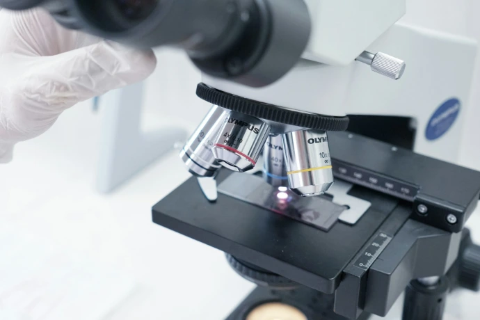 A person in white gloves is looking through a microscope